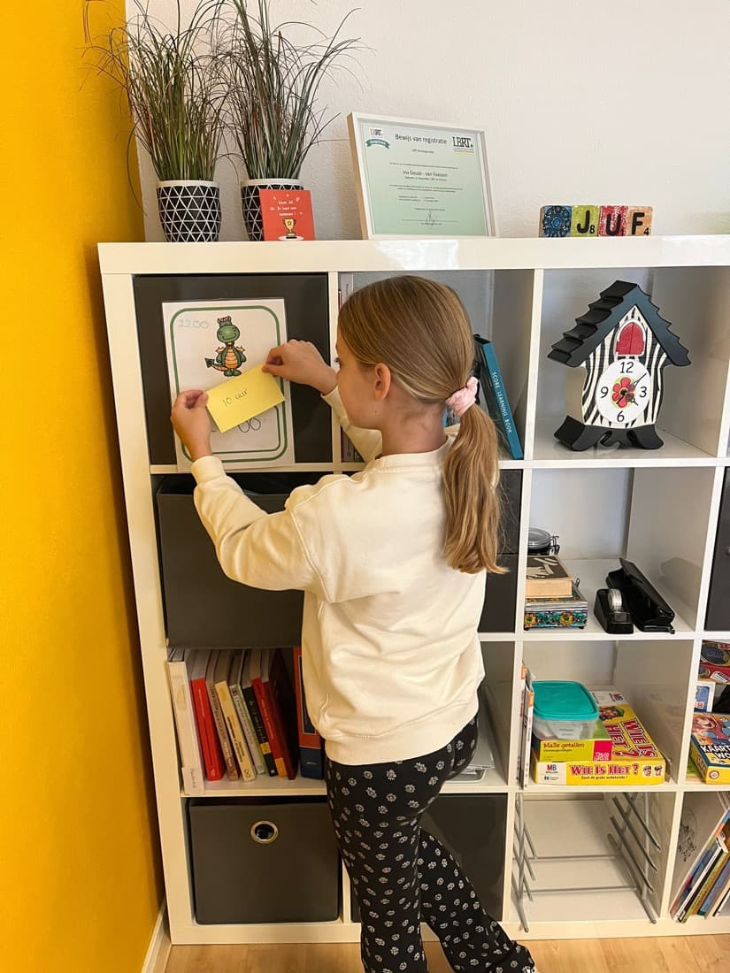 Een meisje hangt een kaartje met een opdracht op in de leerstudio, naast de gele wand.
